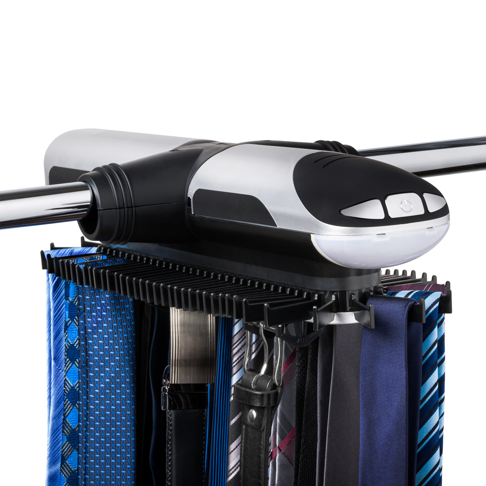 Elektryczny wieszak do krawatów zamontowany na metalowym drążku z szafy. Na wieszaku wiszą krawaty i dwa paski do garnituru.