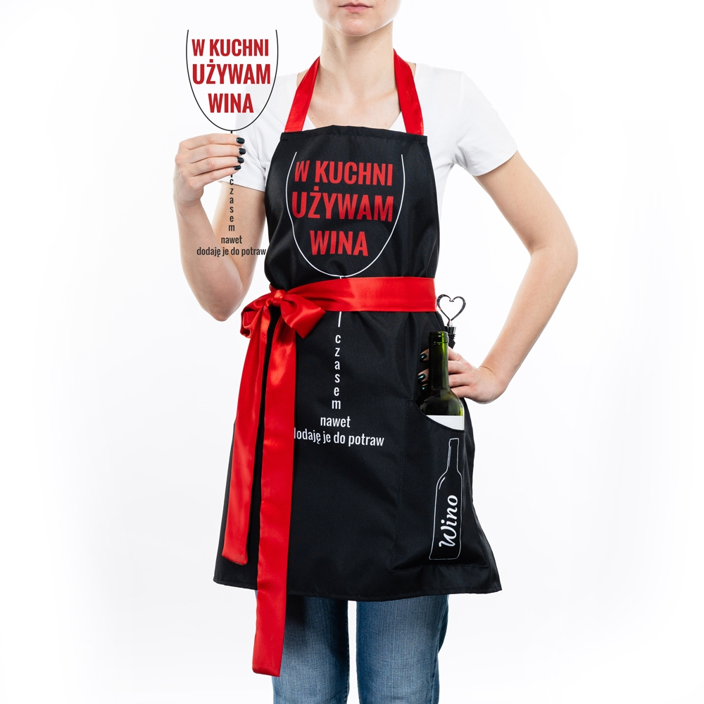 Dziewczyna w fartuszku dla gotującej kobiety, trzymająca w dłoni kieliszek składający się z napisu: w kuchni używam wina, czasem nawet dodaję je do potraw.