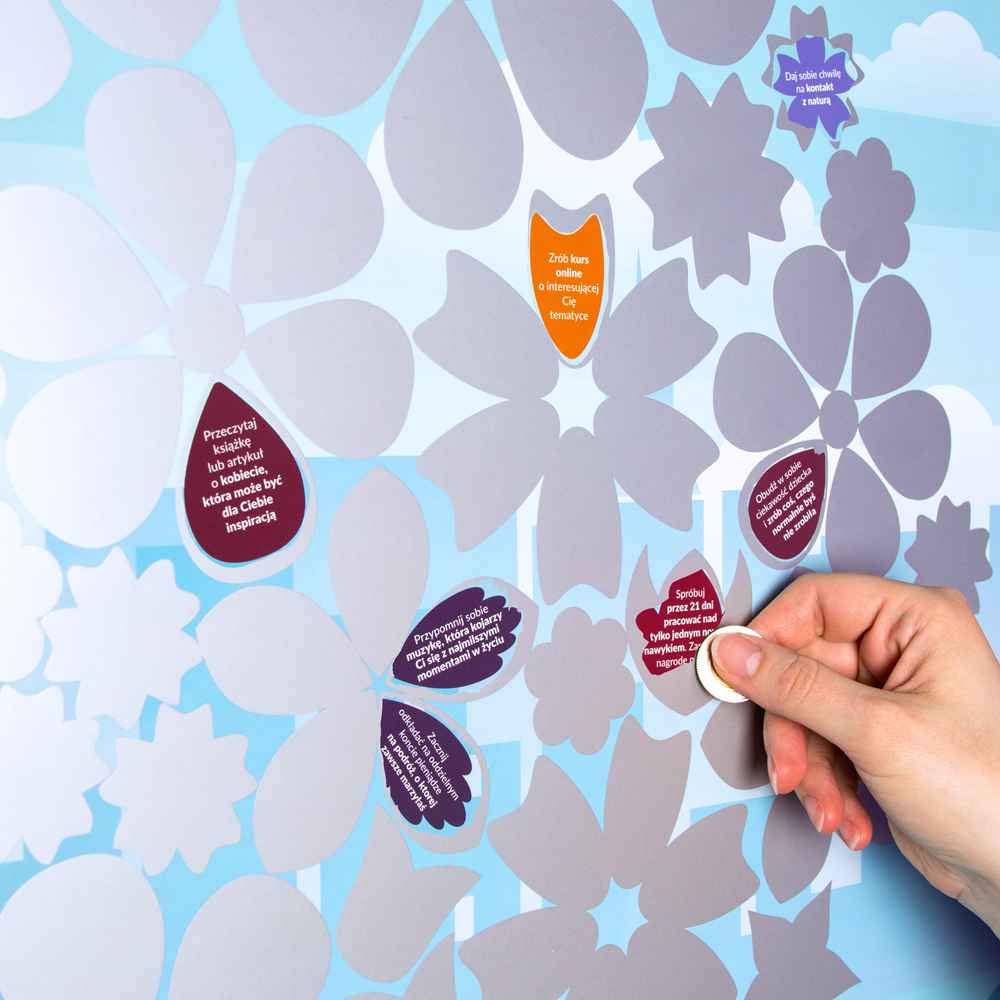 Fragment zdrapki z kilkoma odsłoniętymi kwiatami oraz kobieca ręka z drapująca monetą kolejne zadanie.